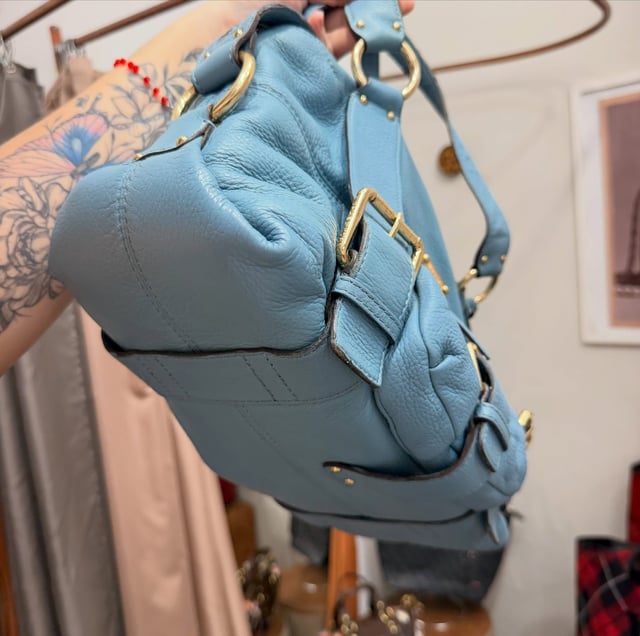 Lateral da bolsa Michael Kors azul-celeste, mostrando a fivela e a argola dourada